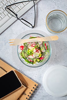 Healthy food in a office. Prepared radish and cucumber salad on a desk with office supplies