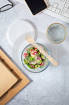 Healthy food in a office. Prepared radish and cucumber salad on a desk with office supplies