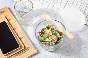 Healthy food in a office. Prepared radish and cucumber salad on a desk with office supplies