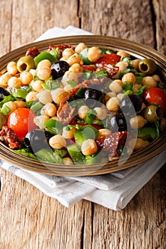 Healthy food: salad balela with chickpeas, tomatoes, onions, olives and herbs close-up. vertical