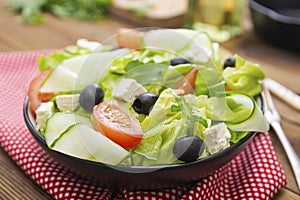 Healthy food. Salad with feta cheese, omatoes, green lettuce and black olives.. Healthy nutrition. Wooden table