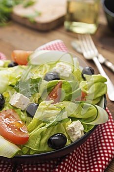 Healthy food. Salad with feta cheese, omatoes, green lettuce and black olives.. Healthy nutrition. Wooden table