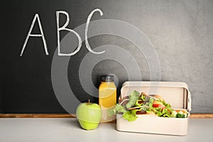 Healthy food for school child in lunch box on table near blackboard