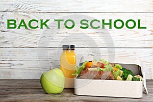 Healthy food for school child in lunch box on table near white wooden wall