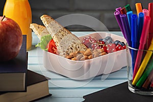 Healthy food for school lunch. On the table among the textbooks is a school lunch, in a box are almonds, red currants