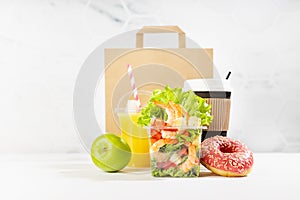 Healthy food set with coffee cup, orange juice, shrimp salad in plastic pack, apple, donut, packet, fruit in white interior.