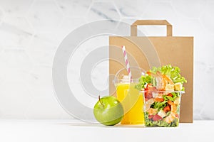 Healthy food set with fresh orange juice, tropical salad with shrimps, vegetables, apple in plastic packaging, packet in white.