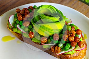 Healthy food - a slice bread dressed with hummus topping, flower-shaped of avocado, green beans, beetroot, roasted peanut.