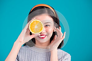 Healthy food. Smiling lovely pinup asian girl holding orange over blue background.