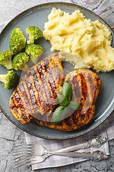 Healthy food spicy grilled chicken breast with a side dish of mashed potatoes and broccoli close-up in a plate on the table.