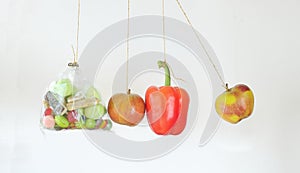 Healthy food versus unhealthful sweets, apples and bell pepper bouncing against bag of junk food, conceptual image, isolated on