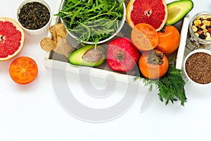 Healthy food in wooden tray: fruits, vegetables, seeds and greens on white background