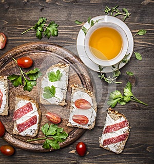 Healthy foods sandwiches with red fish, cherry tomatoes and salami on a cutting board, cup of tea with thyme on wooden rust