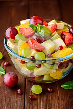 Healthy fresh fruit salad in glass bowl on wooden background.