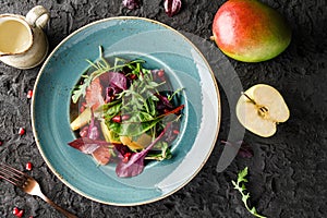 Healthy fresh fruit salad with greens and sauce in bowl over dark background.