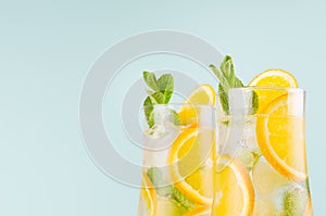 Healthy fresh oranges cocktail with sliced fruit, ice cubes, green mint on elegant soft blue color wall, closeup, top section.