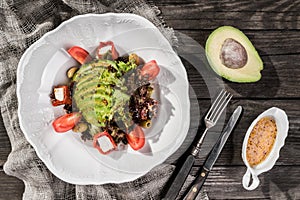 Healthy fresh salad with avocado, greens, arugula, cherry tomatoes, olives and cheese in plate over rustic wooden table