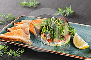 Healthy fresh salad with avocado, salmon, greens, arugula, spinach and cheese with toast in plate over dark background