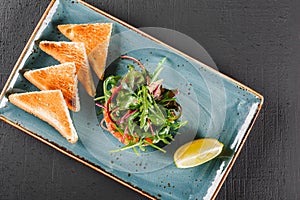 Healthy fresh salad with avocado, salmon, greens, arugula, spinach and cheese with toast in plate over dark background