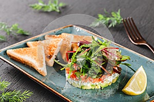 Healthy fresh salad with avocado, salmon, greens, arugula, spinach and cheese with toast in plate over dark background. Healthy