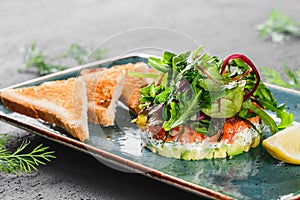 Healthy fresh salad with avocado, salmon, greens, arugula, spinach and cheese with toast in plate over dark background. Healthy