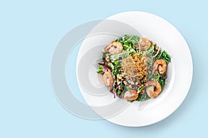 Healthy fresh salad with lettuce, greens, nuts, shrimp and sauce in plate on isolated blue background. Healthy food, clean eating