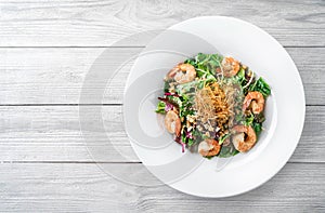 Healthy fresh salad with lettuce, greens, nuts, shrimp and sauce in plate on light wooden background. Healthy food, clean eating,