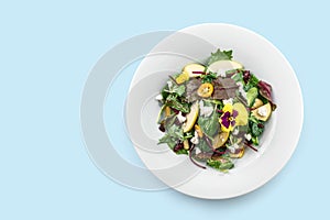 Healthy fresh salad with mix greens, apple, cream cheese, cranberry, sauce and edible flowers in plate isolated on blue background