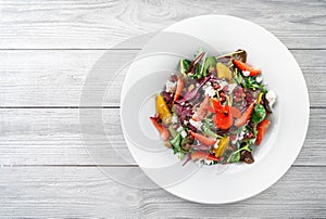 Healthy fresh salad with mix greens, strawberry, orange, nuts, cream cheese and edible flowers in plate on light wooden background