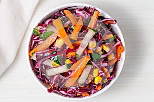 Healthy fresh salad with red cabbage, cucumber, carrot and corn in a bowl on white wooden table. Bright vegetarian food