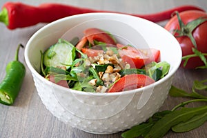 Healthy fresh summer salad with cucumbers, tomatoes, fresh arugula, chopped walnuts, pepper, olive oil and lemon juice