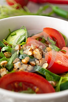 Healthy fresh summer salad with cucumbers, tomatoes, fresh arugula, chopped walnuts, pepper, olive oil and lemon juice