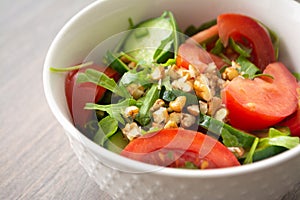 Healthy fresh summer salad with cucumbers, tomatoes, fresh arugula, chopped walnuts, pepper, olive oil and lemon juice