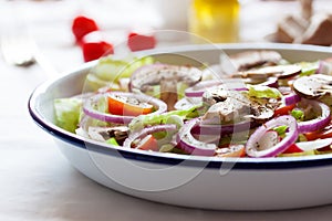 Healthy fresh summer salad with letucce, radish, cherry tomatoes, red onion and champignons with italian herbs on a table