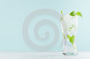 Healthy fresh tonic with green mint, ice cubes, soda, striped straw in misted glass on white wood table, pastel green color .