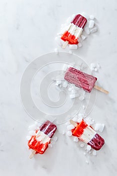 A healthy fruit colored ice cream on a stick with ice cubes on a gray marble table with a copy of the space for text