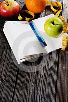 Healthy fruit with notebook for planing in diet concept and weight loss on wooden background