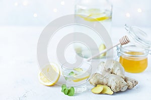 Healthy ginger drink in a cup. Ginger root, honey in a jar, lemon on a white table