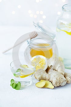 Healthy ginger drink in a cup. Ginger root, honey in a jar, lemon on a white table