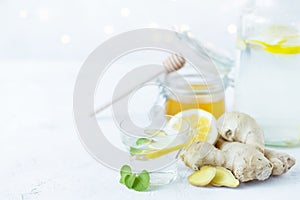 Healthy ginger drink in a cup. Ginger root, honey in a jar, lemon on a white table