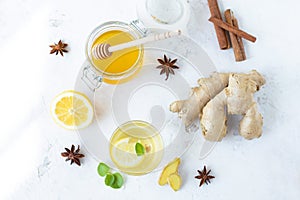 Healthy ginger drink in a cup. Ginger root, honey in a jar, lemon on a white table