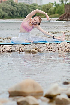 Healthy girl relaxing while meditating and doing yoga exercise in the beautiful nature on the bank of the river