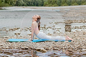 Healthy girl relaxing while meditating and doing yoga exercise in the beautiful nature on the bank of the river