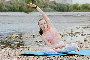 Healthy girl relaxing while meditating and doing yoga exercise in the beautiful nature on the bank of the river