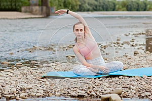 Healthy girl relaxing while meditating and doing yoga exercise in the beautiful nature on the bank of the river