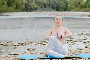 Healthy girl relaxing while meditating and doing yoga exercise in the beautiful nature on the bank of the river