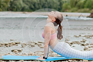 Healthy girl relaxing while meditating and doing yoga exercise in the beautiful nature on the bank of the river