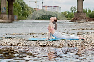 Healthy girl relaxing while meditating and doing yoga exercise in the beautiful nature on the bank of the river