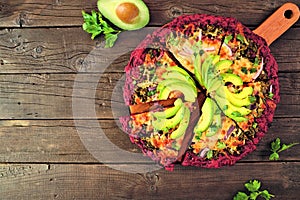 Healthy, gluten free beet crust pizza with avocados, pesto sauce and onions, table scene on dark wood