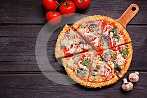 Healthy, gluten free cauliflower crust pizza with tomatoes, mushrooms and spinach. Top down view table scene on dark wood.